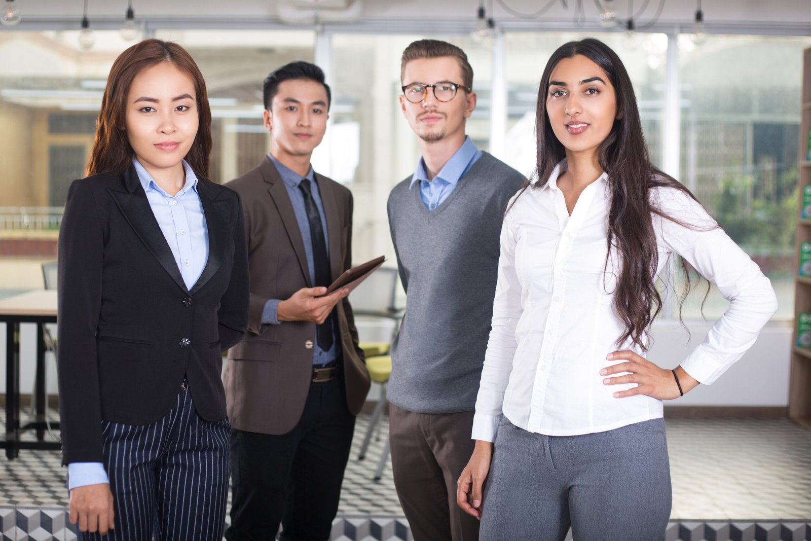 Closeup portrait of four confident young business people looking at camera and standing with cafe interior in background