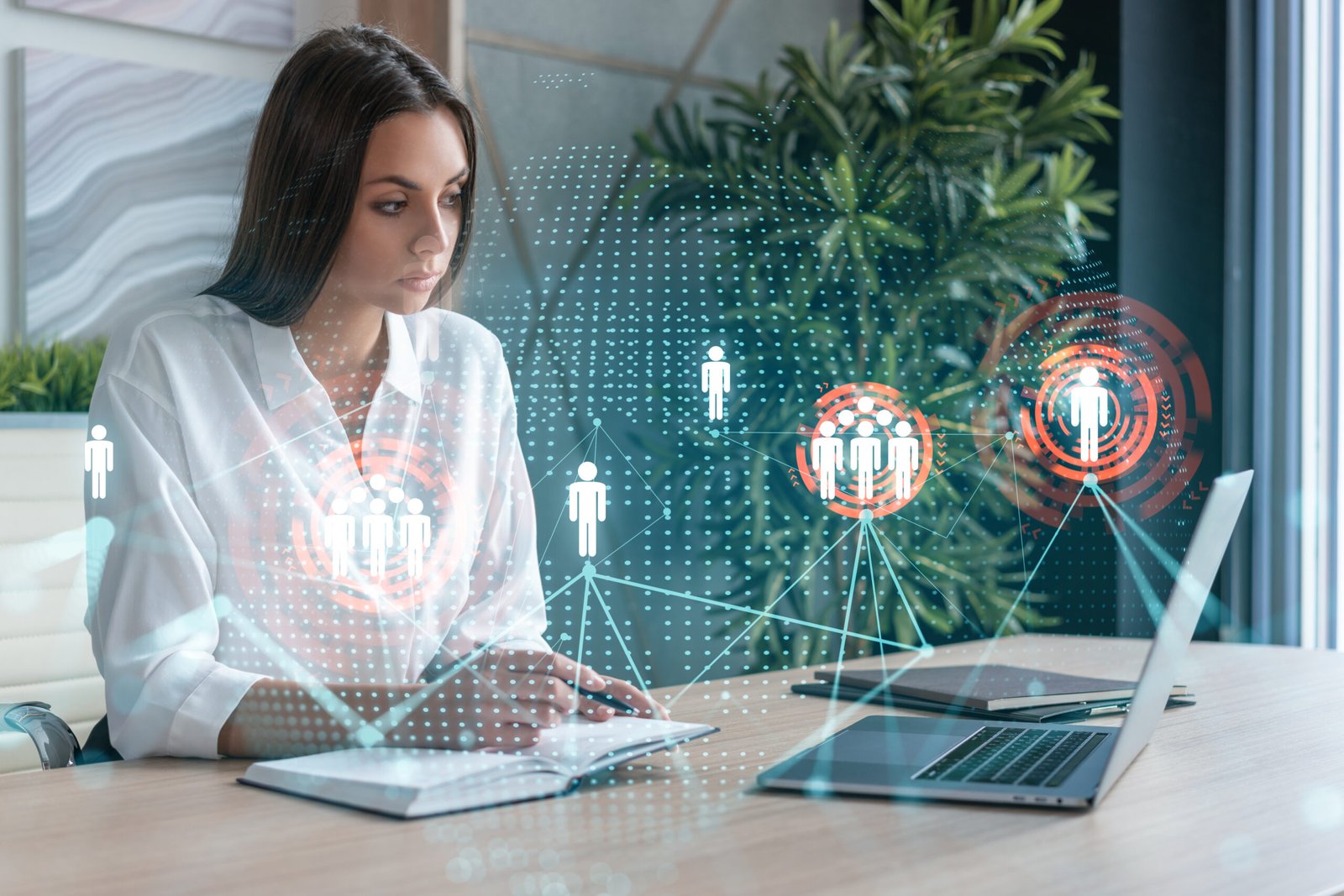 Attractive businesswoman in white shirt at workplace working with laptop to hire new employees for international business consulting. HR, social media hologram icons over office background
